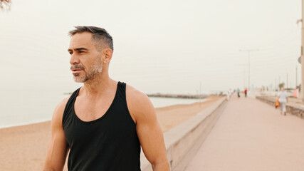 Middle-aged muscular man walks along the promenade before jogging
