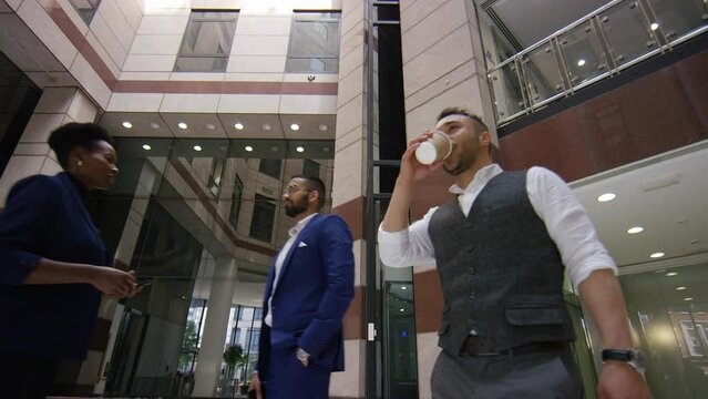 Moving portrait of handsome executive walking through a lobby sipping from a cup, in slow motion