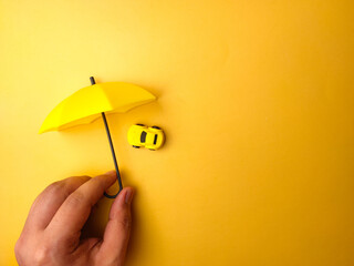 Someone hand holding yellow umbrella covered yellow car