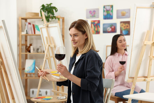 Women with glasses of wine attending painting class in studio. Creative hobby