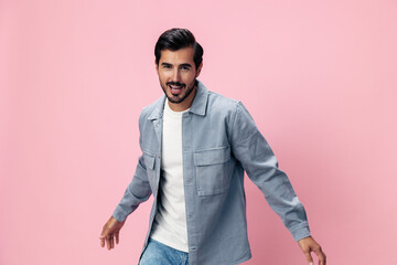 Fototapeta premium Fashion brunette man with beard happiness open mouth jumping and running with his arms spread on a pink background in a white T-shirt and jeans smile and joyful emotion on his face, copy space