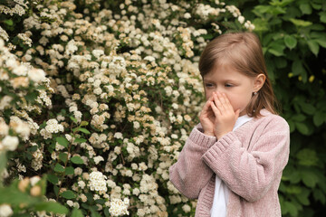 Little girl suffering from seasonal pollen allergy near blossoming tree on spring day