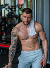 Obraz premium Muscular man workout in the gym. Athletic man having weight training in gym. Handsome man with strong muscles workout in the gym. Portrait of sexy muscular male with dumbbells. Bodybuilder exercise.