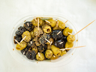 Assortiment d'olives vertes et d'olives noires pour l'apéritif, avec de petits pics en bois, sur une table blanche