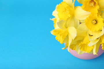 Bouquet of beautiful yellow daffodils in vase on light blue background, above view. Space for text
