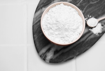 Bowl and spoon of natural starch on white tiled table, top view. Space for text