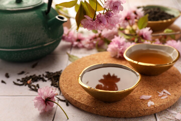 Obraz na płótnie Canvas Traditional ceremony. Cup of brewed tea, teapot, dried leaves and sakura flowers on tiled table, closeup