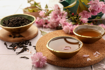 Traditional ceremony. Cup of brewed tea, teapot, dried leaves and sakura flowers on tiled table, closeup