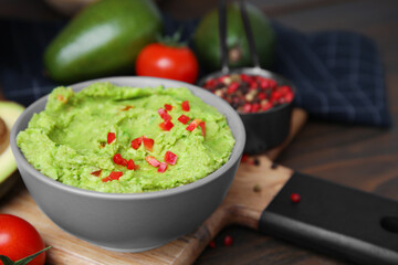 Bowl of delicious guacamole and ingredients on wooden table, closeup. Space for text