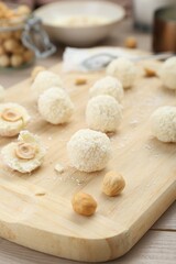 Delicious candies with coconut flakes and hazelnut on wooden board, closeup