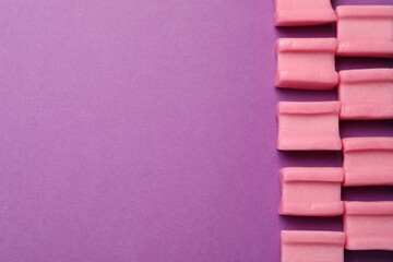 Tasty pink chewing gums on purple background, flat lay. Space for text