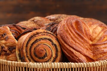 Wicker basket with different tasty freshly baked pastries on blurred background, closeup