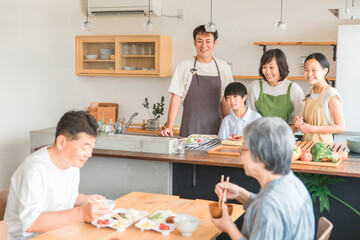 家のダイニングで祖父母に料理を作る孫・親子（二世帯住宅）
