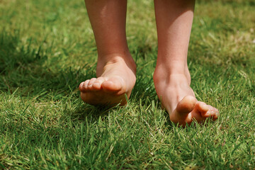 Happy child is barefoot on the grass, close-up feet, enjoying sunny summer day during vacation....