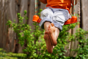 Boy crossed his bare feet. Closeup of feet happy kid sitting and swinging, sunny summer day,...