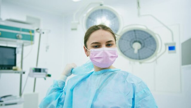 Portrait of a young female doctor in sterile protective clothing removing a mask in the operating room after an operation