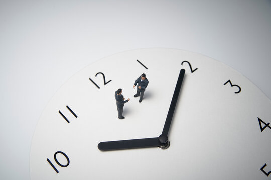 時計の上で打ち合わせするミニチュアのビジネスマン