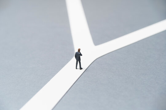 分かれ道の前で悩むミニチュアのビジネスマン