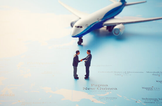 世界地図の上の飛行機と握手をするミニチュア