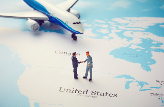 世界地図のアメリカの上で握手をするミニチュア人形と飛行機