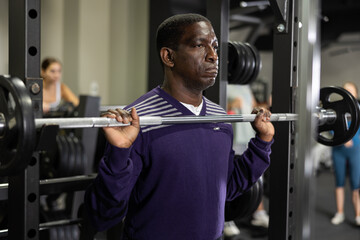 Fototapeta na wymiar African man doing squats with weight using half rack in gym