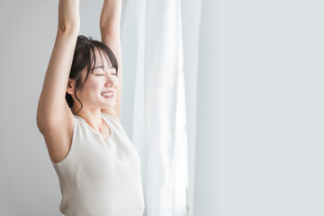 寝起き・起床時にカーテンの前で朝日を浴びる女性（脱毛・脇）
