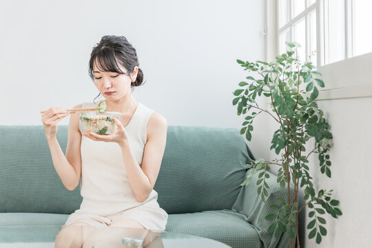家でサラダを食べるダイエット中の若いアジア人女性（好き嫌い・困る・悩む）
