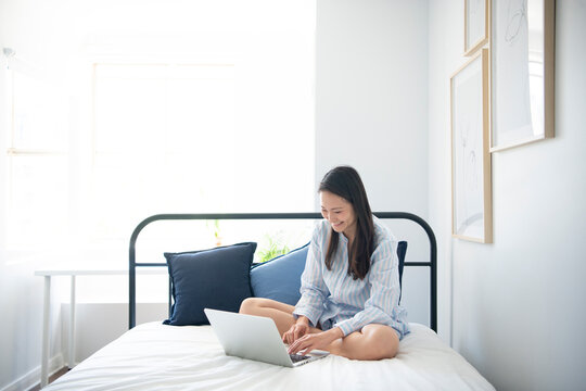 ベッドの上でパソコンを触っているパジャマ姿の女性