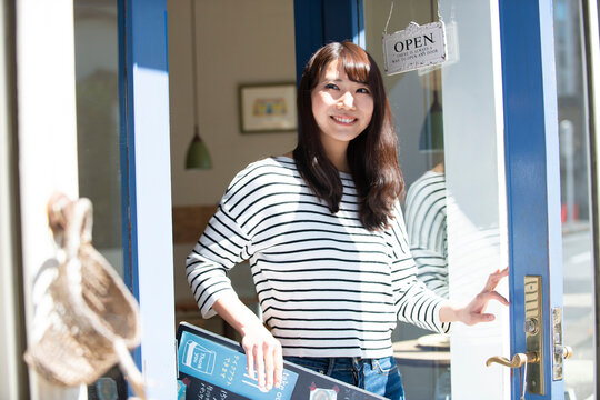 お店の前で看板を持って笑っている女性