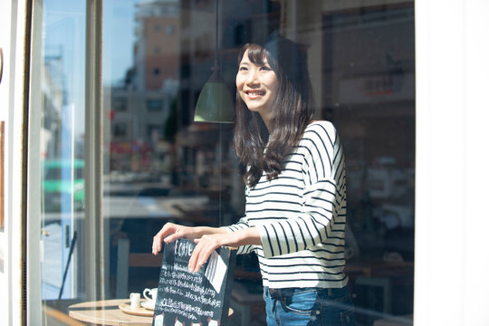 お店の中で看板を持って笑っている女性