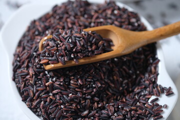 raw black rice in a white ceramic bowl. purple rice. Oryza sativa L. indica. carbohydrate. staple food. beras Hitam.