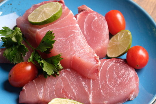 Fish filet is fish meat that has been cut or sliced away from the bone by cutting lengthwise along one side of the fish. on a brown wooden cutting board. cherry tomato, lime. Istiompax indica. Marlin