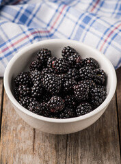 Blackberries in ceramic bowl on rustic wooden background. Selective focus. Shallow depth of field.