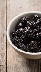 Blackberries in ceramic bowl on rustic wooden background. Selective focus. Shallow depth of field.