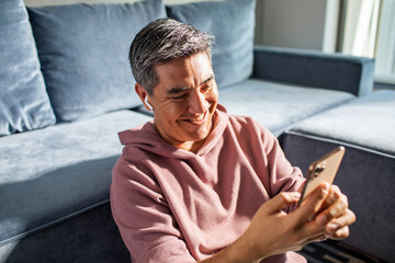 MIddle aged latin man using a smart phone on a couch at home