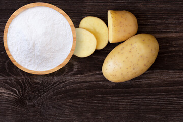 Potato powder in wooden bowl and fresh potatoes with slice isolated on wooden table background. Top view. Flat lay.