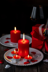 Saint Valentine's Day celebration. Red burning candles, hearts, gift box, postcard on dark wooden background. Happy holiday . Table decor for festive dinner, romantic atmosphere. Copy space for text
