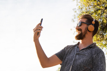 Young happy man taking selfie with mobile phone outdoors. Copy space.