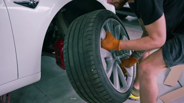 Auto mechanic man changing a wheel on a luxury white car using a balloon wrench at a car service station close-up