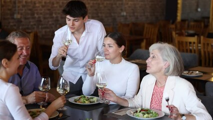 Large, friendly family, company of spouses in restaurant, eat, celebrate important event, communicate. Cozy sparsely populated restaurant, festive lunch, wine tasting