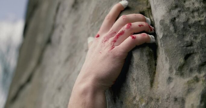 Bloody and taped climber hand grips onto gap in mountain wall trying not to fall.