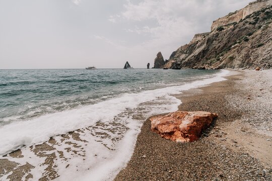 Large red jasper rock on the beach, with the sea in the background. Big Red Jasper Stone Close Up