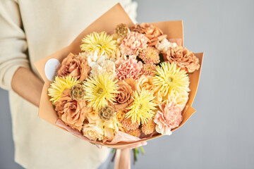 a beautiful bouquet of fresh flowers in the hands of a florist. A gift bouquet in a peach color scheme for any holiday. A very nice female florist is holding a beautiful colorful bouquet of fresh - 609812745