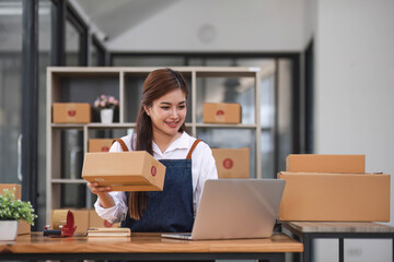 Fototapeta na wymiar Startup happy Asian woman business owner works with a box at home office. prepare parcel delivery SME supply chain, procurement, package box to deliver to customers,