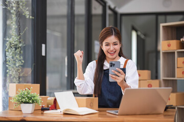 Startup SME small business entrepreneur of freelance Asian woman using a smartphone with box Cheerful success Asian woman her hand lifts up online marketing packaging box and delivery SME