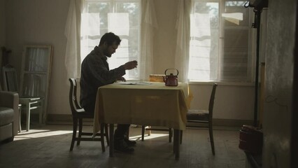 Full shot of white man reading with coffee at table in antique room. Side view