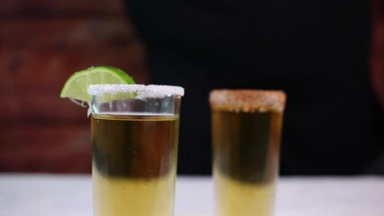 close-up of bartender placing lemon slices into two shots of golden tequila in slow motion