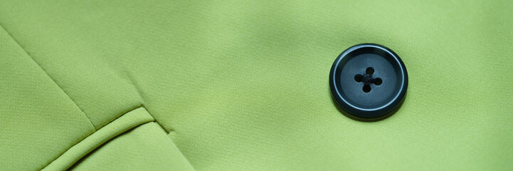 Black button is sewn on green cotton fabric closeup. Buttons for clothes features and selection