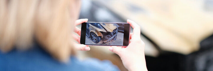 Female insurance agent takes photo of burnt-out car on phone. Evidence of car arson and felony - obrazy, fototapety, plakaty