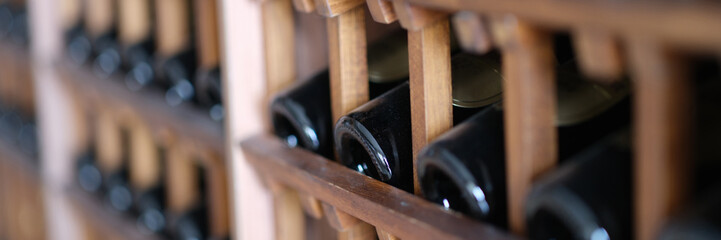 Resting dusty wine bottles stacked on wooden racks in basement. Elite collectible expensive wine in...